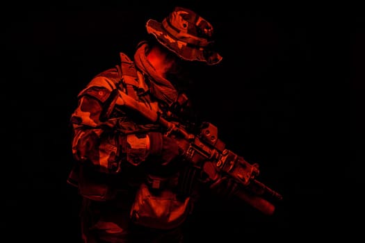 Commando shooter, army special forces rifleman in battle uniform, boonie hat, ammunition in load carrier, camouflaged with paint face, armed assault rifle, half length toned colorized portrait on black background