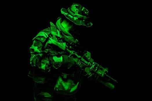Commando shooter, army special forces rifleman in battle uniform, boonie hat, ammunition in load carrier, camouflaged with paint face, armed assault rifle, half length toned colorized portrait on black background
