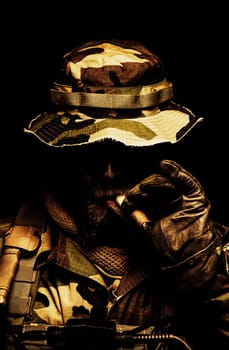 Brutal and serious commando soldier, army special forces veteran, in camouflage battle uniform, boonie hat, black paint on bearded face, combat knife in shoulder holder, smoking cigar, studio portrait toned and colorized