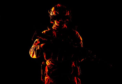 Half length, low key studio shoot of army soldier, marine infantryman in mask, camo uniform, equipped modern ammunition, armed service rifle standing in darkness with night vision device on helmet