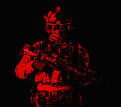 Half length, low key studio shoot of army soldier, marine infantryman in mask, camo uniform, equipped modern ammunition, armed service rifle standing in darkness with night vision device on helmet