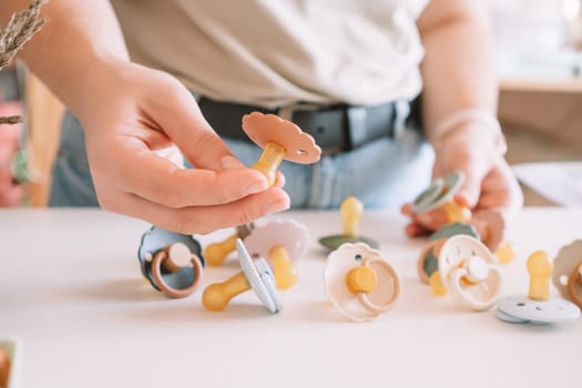 Cropped business woman hands, making and design craft silicone pacifiers for newborn babies on white desk. Small business, store. Choosing soft material for kids. Natural ecological accessories.