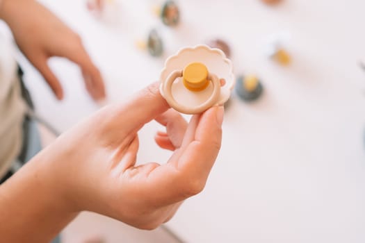 Cropped business woman hands, making and design craft silicone pacifiers for newborn babies on white desk. Choosing colors and shape for kids. Small business, store. Natural ecological accessories.