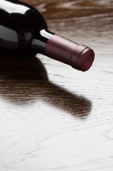 Red Wine Bottle Laying on a Wood Surface Fading Down to White.