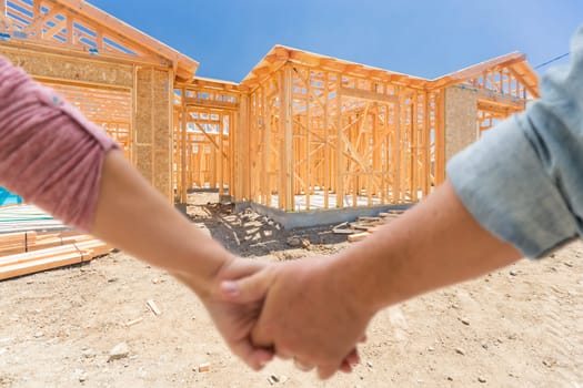 Couple Holding Hands Looking At Their New House Framing Under Construction.