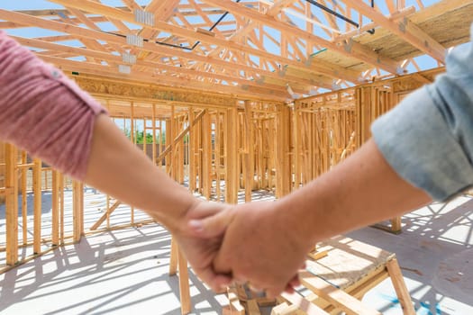 Couple Holding Hands Looking At Their New House Framing Under Construction.