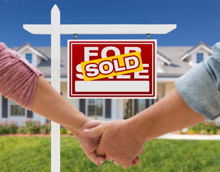 Couple Holding Hands In Front of Beautiful New House and Sold For Sale Real Estate Sign.