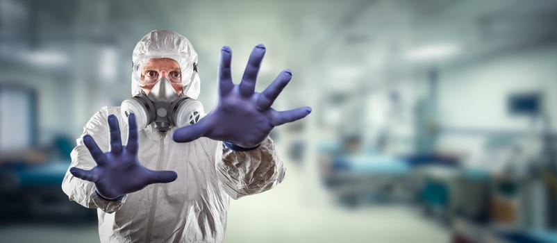 Man Wearing Hazmat Suit, Protective Gas Mask and Goggles Reaching To Stop with Hands Within Hospital.