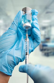 Doctor or Nurse Wearing Surgical Gloves Holding Vaccine Vial and Medical Syringe Within Hospital.