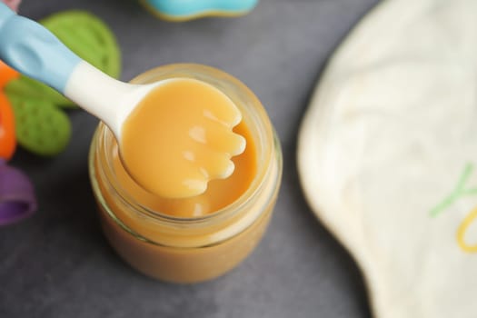 A colorful spoon is dipped into a jar of creamy baby food on a table.