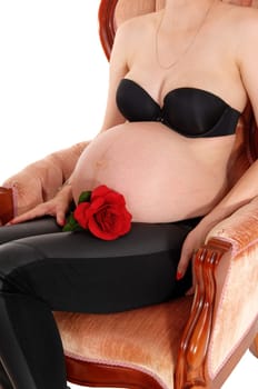 A high pregnant woman sitting in a pink armchair wit a red rose at her.belly, isolated for white background..
