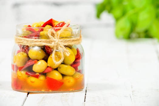 glass jar with olives and peppers on old white table