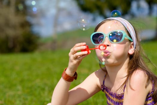 a little girl with sunglasses making soap bubbles