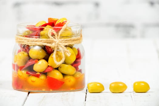 glass jar with olives and peppers on old white table