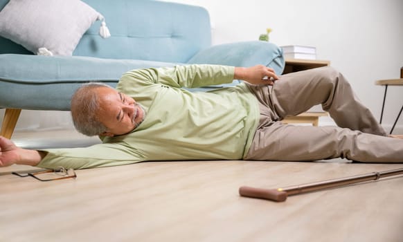 Asian old man lying on floor after falling down with wooden walking stick, Sick senior man beside couch on rug in living room at home, Elderly having an accident after doing physical therapy alone