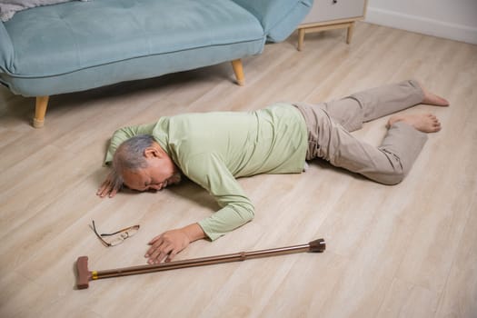 Asian senior man falling down lying on floor at home alone with wooden walking stick in living room, Elderly man headache after fall down, Health care and medicine concept