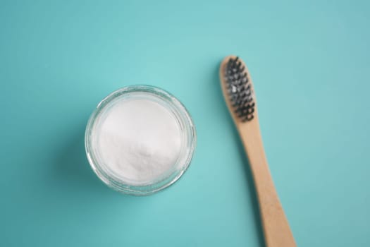 A jar of baking soda and a toothbrush on a teal surface showing dental care.