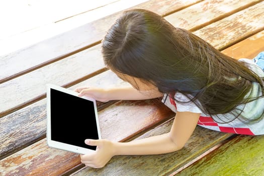 The girl lying on wooden bed with playing tablet pc.