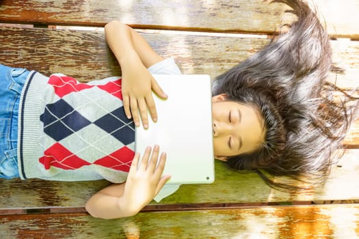 The girl sleep while playing tablet pc on wooden bed.