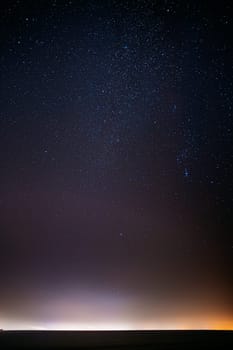 Night Starry Sky With Glowing Stars Above Countryside Landscape. Milky Way Galaxy And Rural Field Meadow In Early Spring. Bright Glowing Stars.