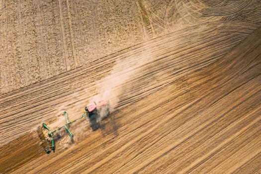 Aerial View. Tractor Plowing Field. Beginning Of Agricultural Spring Season. Cultivator Pulled By A Tractor In Countryside Rural Field Landscape. Dust Rises From Under Plows.