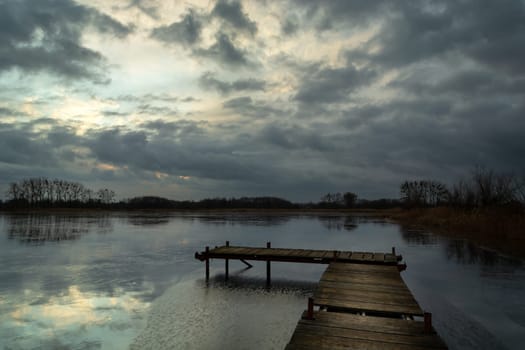 A pier on a frozen lake and dark clouds, winter view