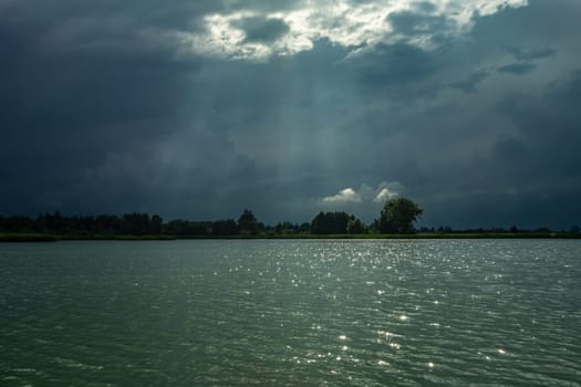 Dark clouds and sunbeams above the lake water, summer evening