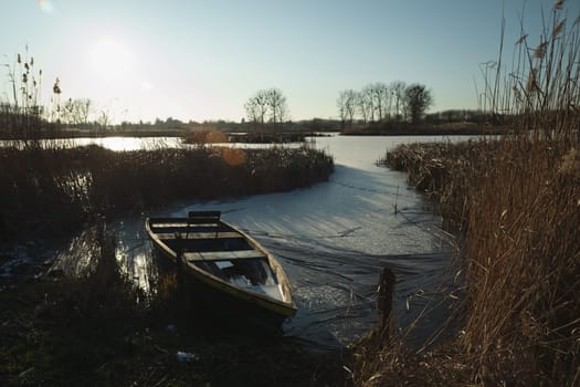 A boat at the edge of a frozen lake, sunny winter day