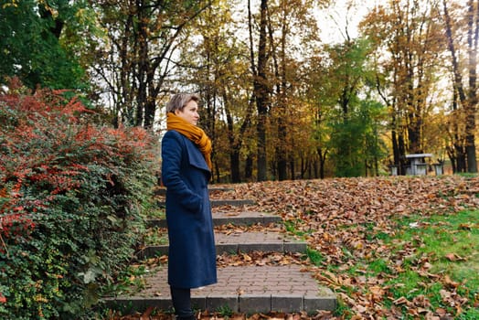Side portrait of a short-haired blonde in a coat and scarf in autumn.