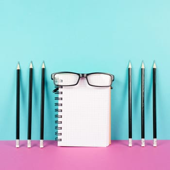 Empty notebook with a pencils and eyeglasses on a pink and blue background, brainstorming for new ideas, writing a message, home office desk