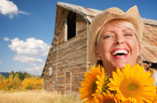 Beautiful Caucasian Young Woman Wearing Cowboy Hat Holding Sunflower In Front of Rustic Barn In The Country.