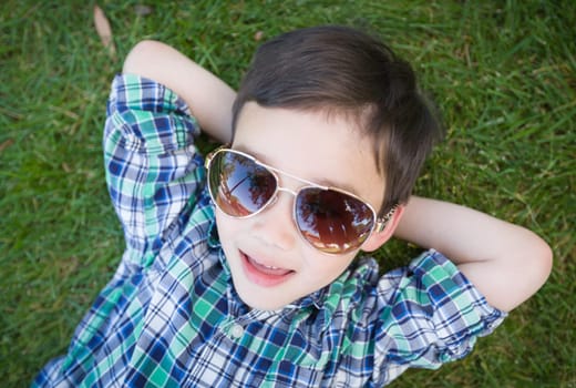 Mixed Race Chinese and Caucasian Young Boy Wearing Sunglasses Relaxing On His Back Outside On The Grass.