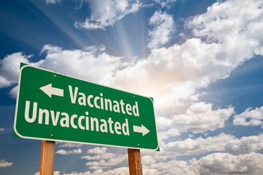 Vaccinated, Unvaccinated Green Road Sign Against Dramatic Clouds and Sky.