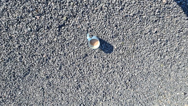 Blue coffee cup with fresh coffee stands on the floor, surrounded by small gray pebbles