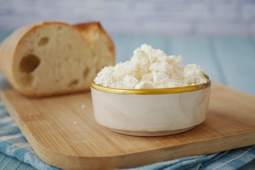 Cottage cheese served in a bowl next to fresh bread on a cutting board.