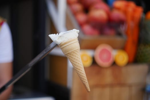 A person serves a scoop of creamy ice cream in a cone at a market.