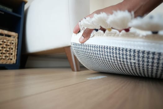 Individual is smoothing a woven rug on a wooden floor indoors while sitting.