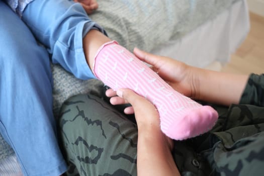 Hands assist in carefully dressing a child in soft pink socks.