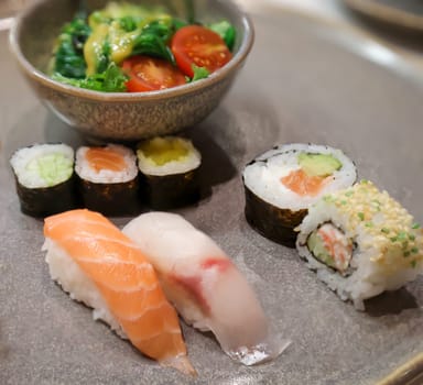 A plate of salad and sushi rolls, fresh raw fish.