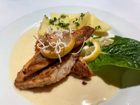 A plate of fried pike perch fillet, with potatoes and lemon.