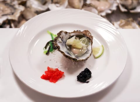 On a plate is an opened oyster with caviar and lemon.