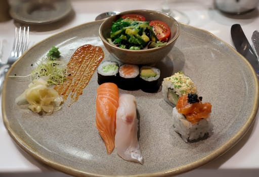 A plate of salad and sushi rolls, fresh raw fish.