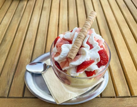 A strawberry sundae with whipped cream and waffle is on a table.