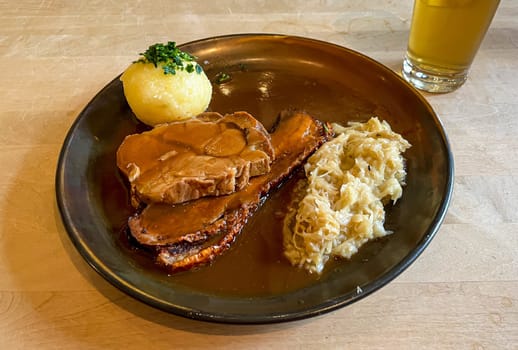 A plate with different pieces of roast pork, dumplings and sauerkraut.