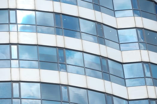 Curved glass windows of a modern building reflect clouds and light.
