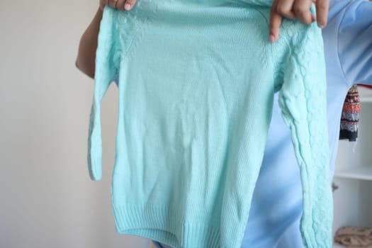 A person displays a mint green sweater in a well-lit indoor space.
