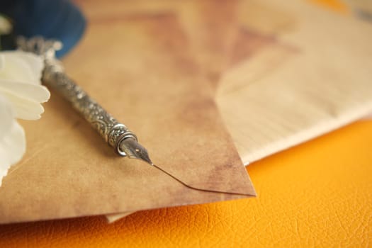 A vintage fountain pen lies on rustic parchment with a flower nearby.