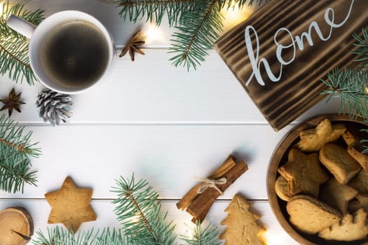Home lettering burnt wood sign, gingerbread cookie, Christmas tree branches, cup of coffee, cinnamon sticks on white surface. Flat lay. Copy space.