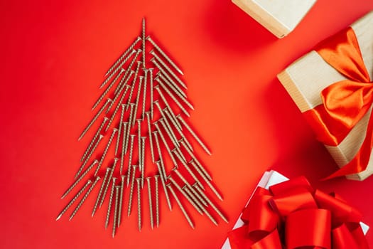 Long golden self-tapping screws, laid out in shape of Christmas tree and gift boxes on red background