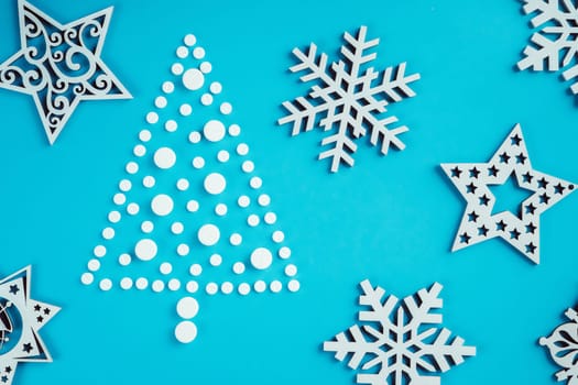White round pills, laid out in shape of Christmas tree with wooden snowflakes on light blue background. Flat lay
